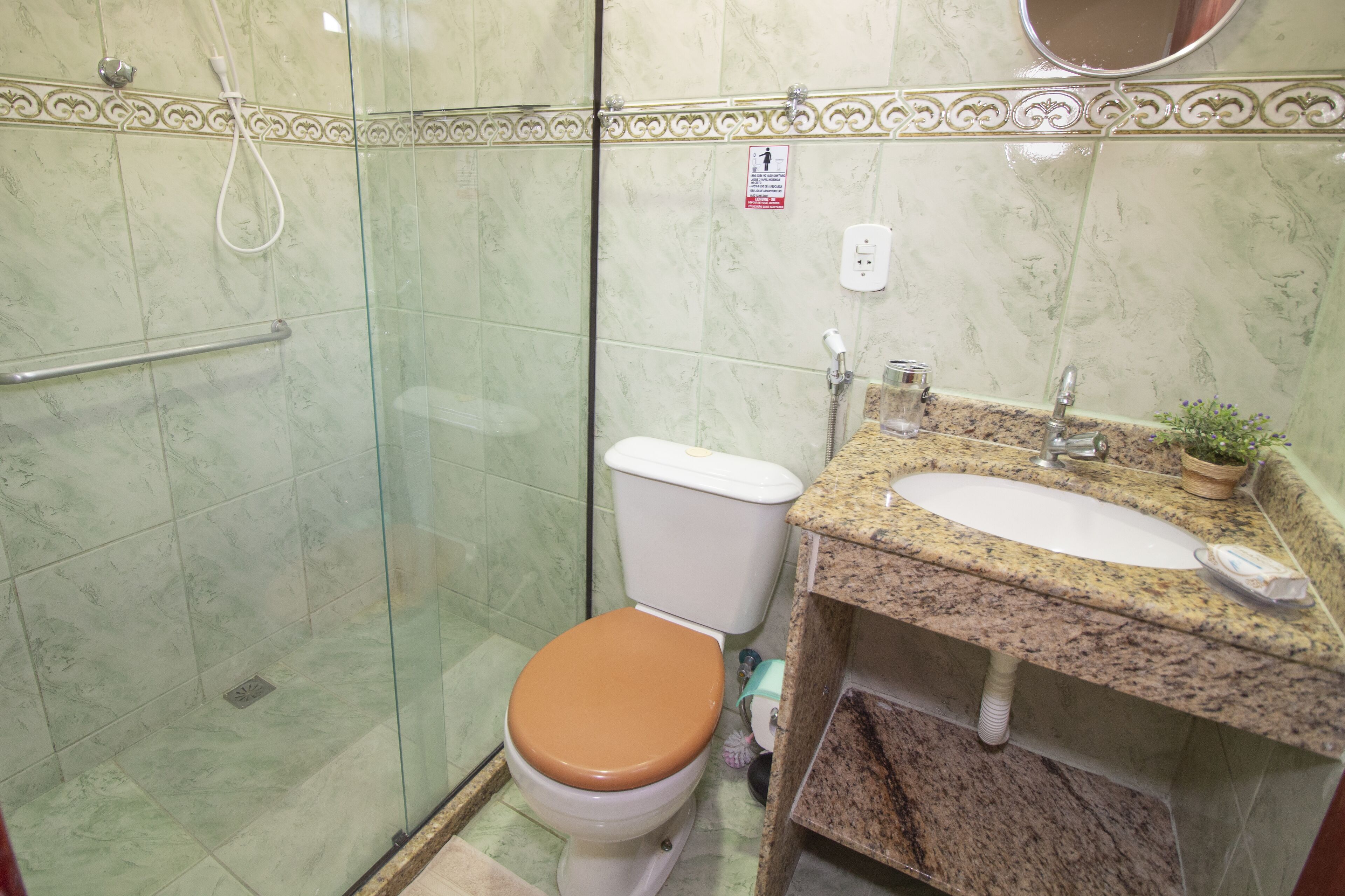 Un baño con ducha de vidrio, inodoro con asiento marrón y lavamanos con encimera de granito.
