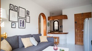 A living room with a grey sofa, a white coffee table, and a kitchen area with wooden cabinets and a refrigerator. - Apartamanto with terrace, free WiFi, communal pool in Puerto Rico (Mogán)