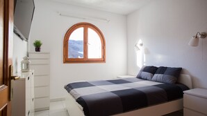 A bedroom with a bed, a bedside table, a lamp, a window, and a small plant. - Apartamanto with terrace, free WiFi, communal pool in Puerto Rico (Mogán)