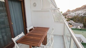 A balcony with a wooden table and white chairs, overlooking a coastal town. - Apartamanto with terrace, free WiFi, communal pool in Puerto Rico (Mogán)