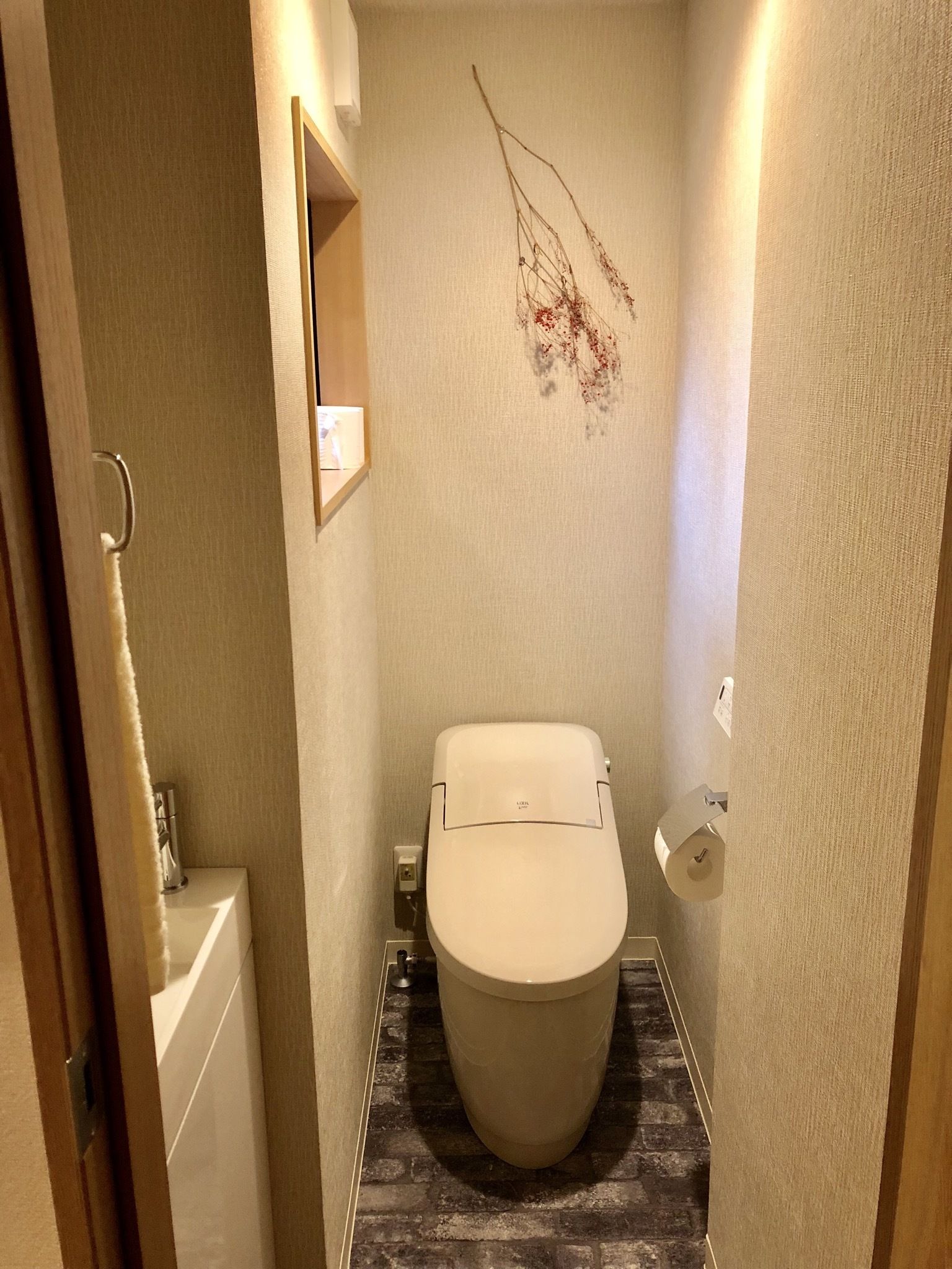 A compact bathroom with a toilet, a small sink, and a decorative branch on the wall.