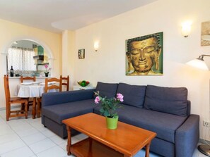 Un salon comprenant un canapé, une table basse en bois, une table à manger avec des chaises, et un tableau représentant un Bouddha accroché au mur.
