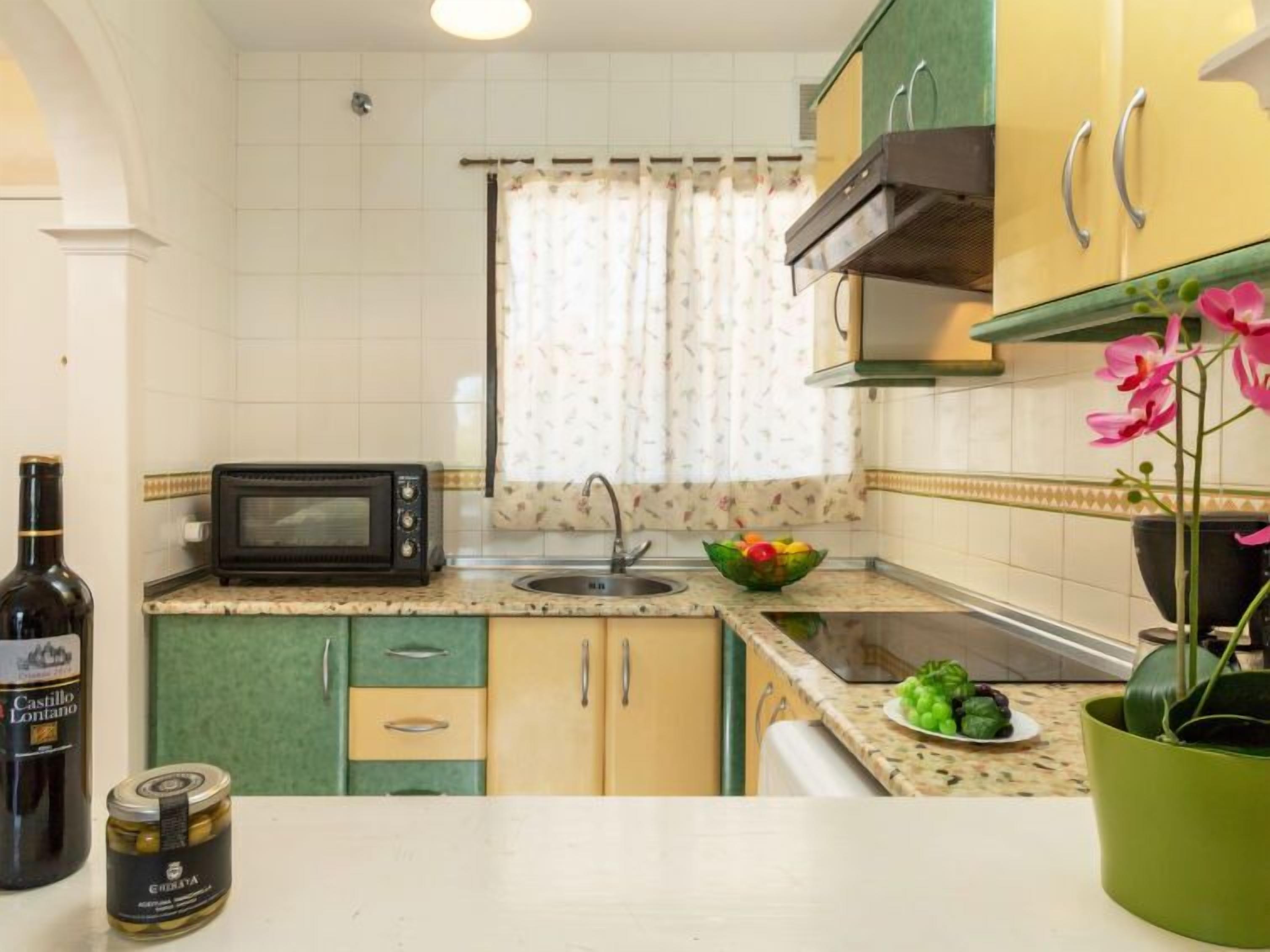 Eine kleine Küche mit Mikrowelle, Spüle und einem Fenster mit Blumenvorhängen.