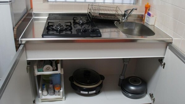 A kitchen with a gas stove, sink, and storage cabinets. - Yenn's Marina Inn Zamami Condominium (Zamami)