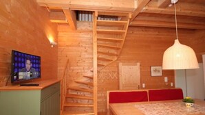 A wooden interior with a staircase, a dining table with red cushions, and a television on a cabinet.