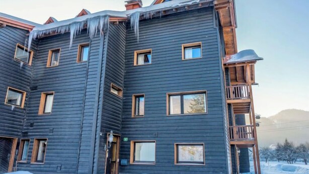 A multi-story log cabin with a dark exterior, multiple windows, and a wooden balcony.