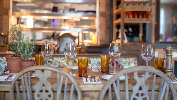 A restaurant setting with a wooden table set for dining, potted plants, and a variety of glassware. - Black Horse (Arundel)
