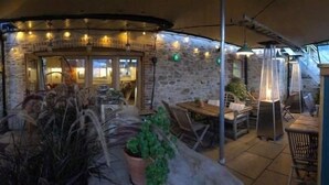 An outdoor patio area with stone walls, wooden furniture, and string lights. - Black Horse (Arundel)