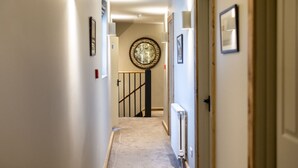 A hallway with a staircase, a radiator, and framed pictures on the walls. - Black Horse (Arundel)
