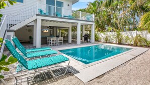 Una casa de dos pisos con un porche cubierto, piscina y mobiliario de exterior.