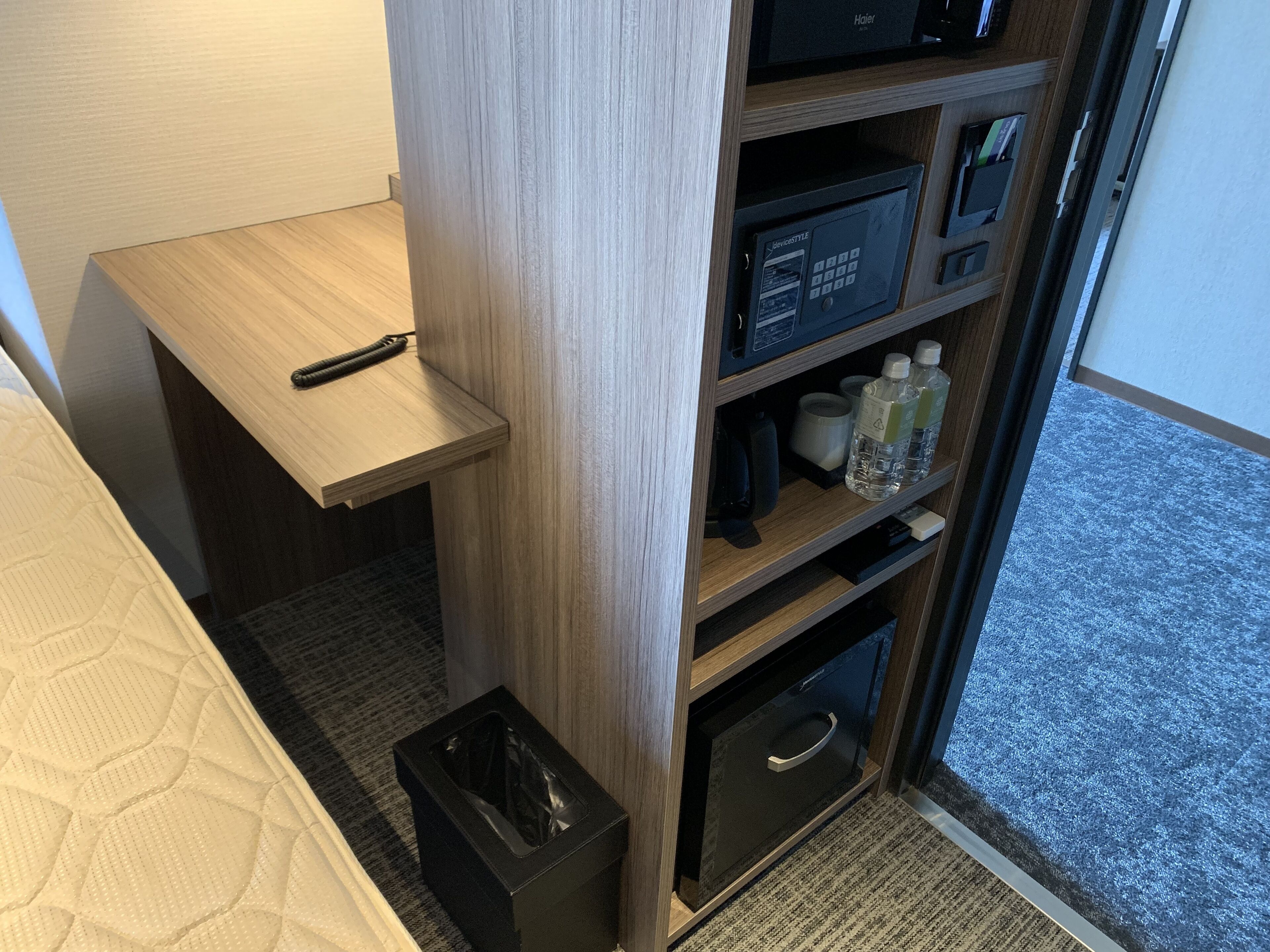 A hotel room with a wooden desk, a minibar, a trash bin, and a carpeted floor.