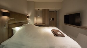 A hotel room with a large bed, a bedside table, a TV, and a bathroom with a mirror and sink. - Hotel H2 Nagasaki (Nagasaki)