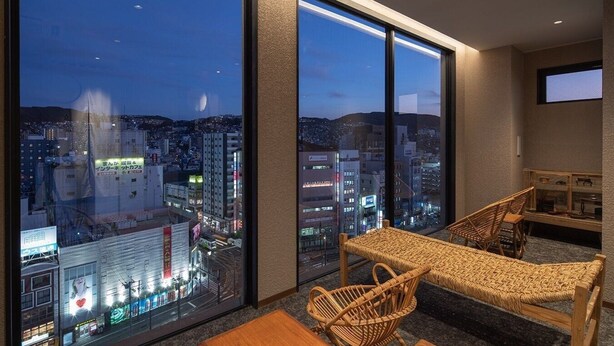 A modern hotel room with large windows offering a city view, a small table, wicker chairs, and a television. - Hotel H2 Nagasaki (Nagasaki)