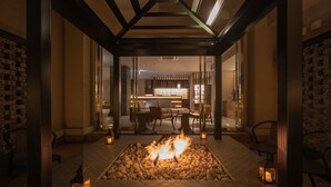 A cozy indoor seating area with a central fire feature, surrounded by tables and chairs, and a visible bar area in the background. - Hotel H2 Nagasaki (Nagasaki)