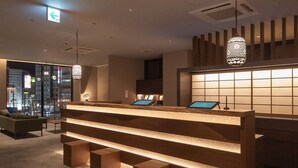 A modern reception area with a wooden reception desk, multiple seating options, and a city view through large windows. - Hotel H2 Nagasaki (Nagasaki)