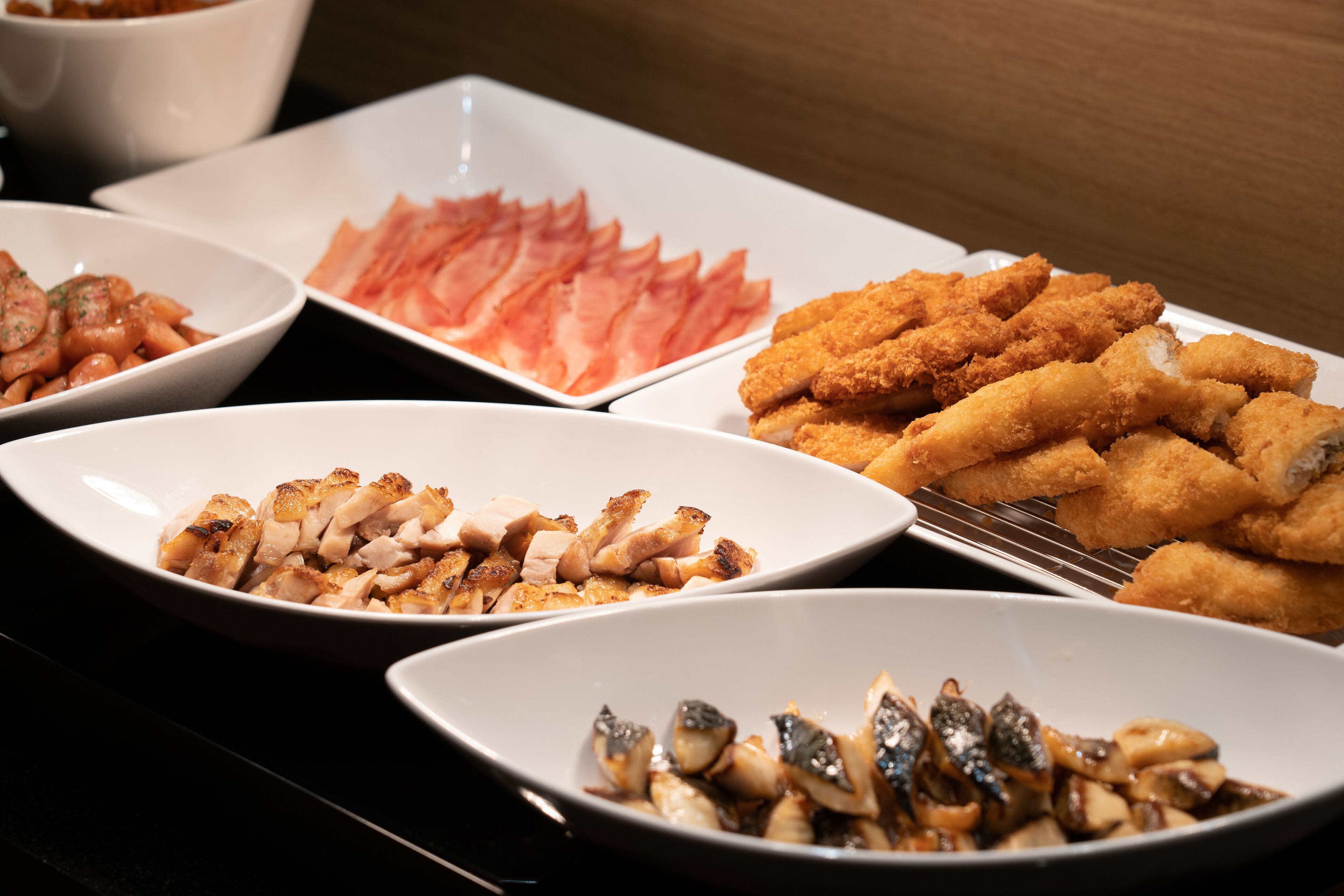 Un bufé con diversos platos, incluyendo carne en rodajas, preparaciones empanizadas y mariscos.