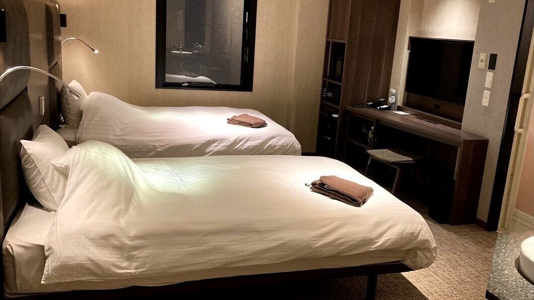 Ein Hotelzimmer mit zwei Betten, einem Fernseher und einer kleinen Sitzecke.