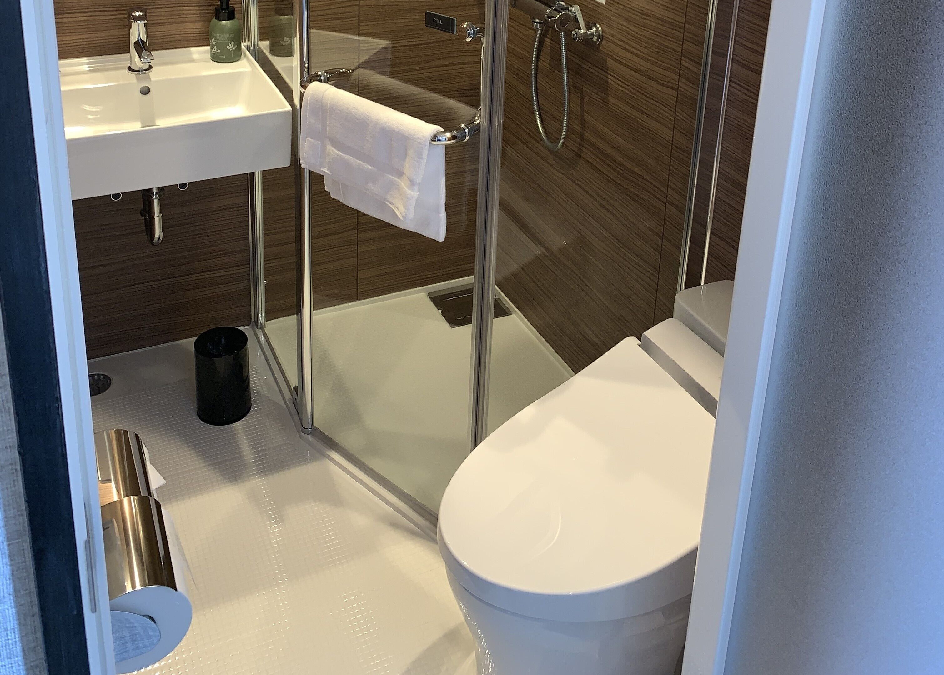 A modern bathroom with a glass-enclosed shower, a white toilet, and a sink with a towel hanging on the wall.