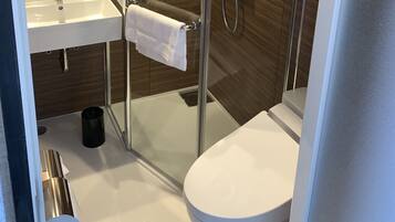 A modern bathroom with a glass-enclosed shower, a white toilet, and a sink with a towel hanging on the wall.