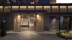 A modern hotel entrance with a geometric patterned gate, a bench, and a stone pathway leading to the entrance. - Hotel H2 Nagasaki (Nagasaki)