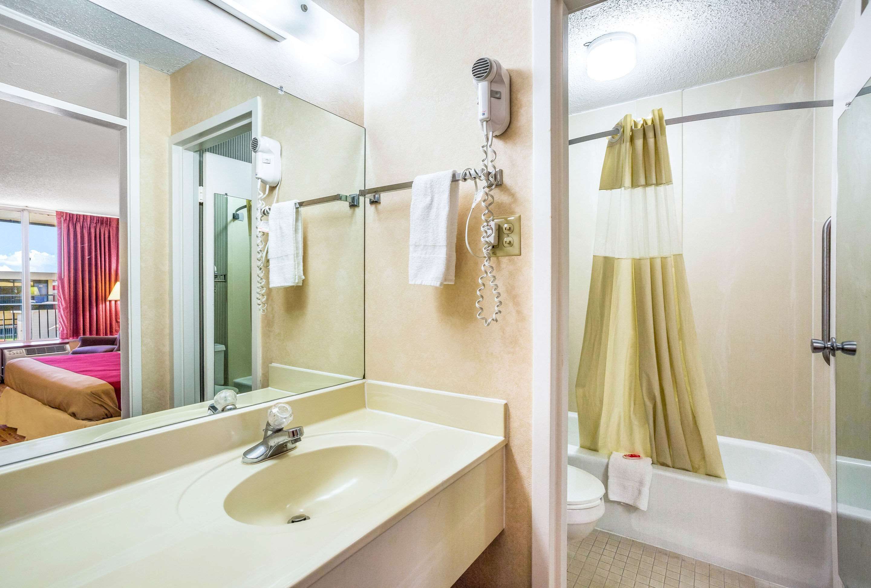 A hotel bathroom with a sink, mirror, hairdryer, and a shower with a curtain.