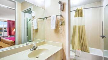 A hotel bathroom with a sink, mirror, hairdryer, and a shower with a curtain.