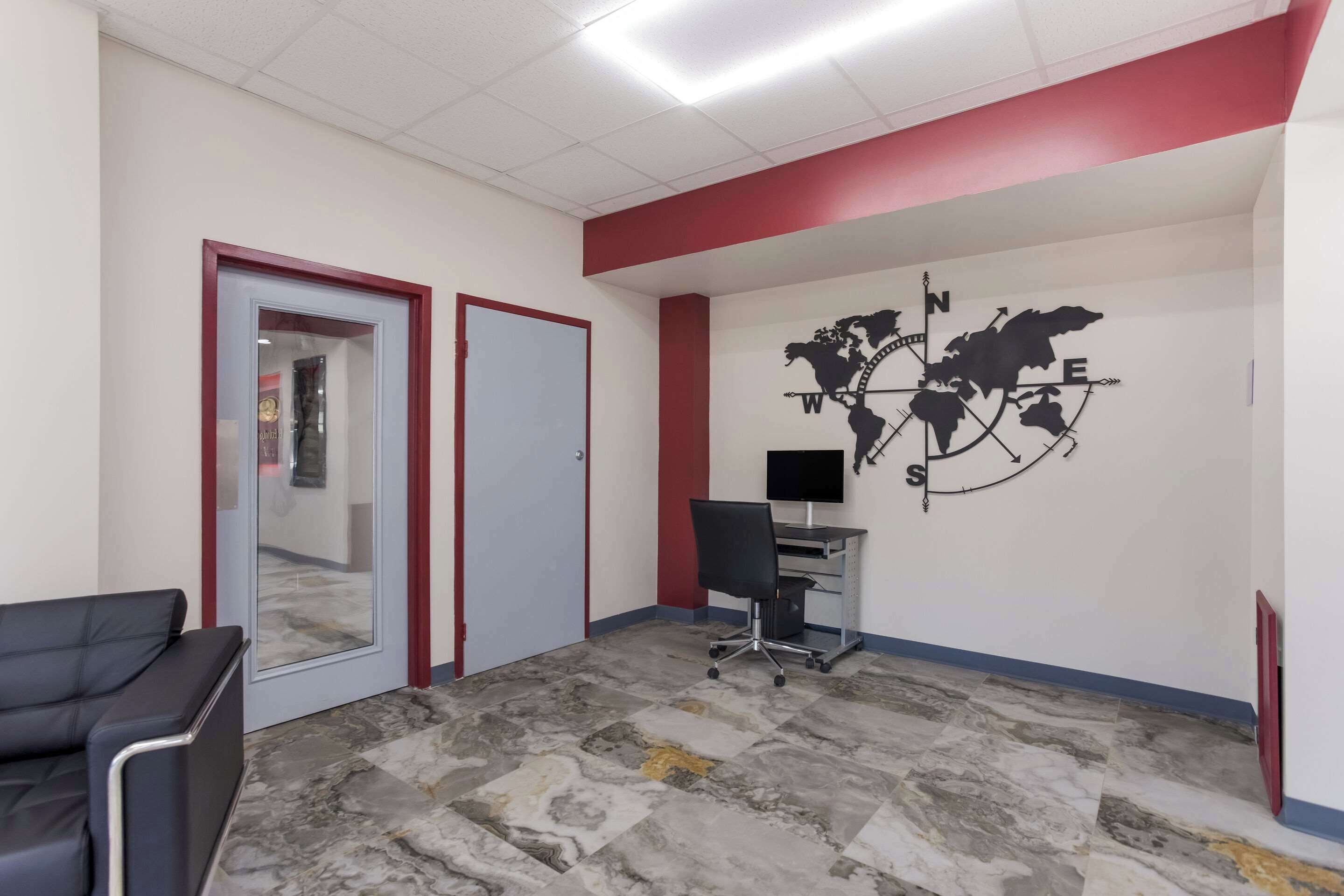 A waiting area with a desk, a black office chair, a red-framed door, and a world map on the wall.
