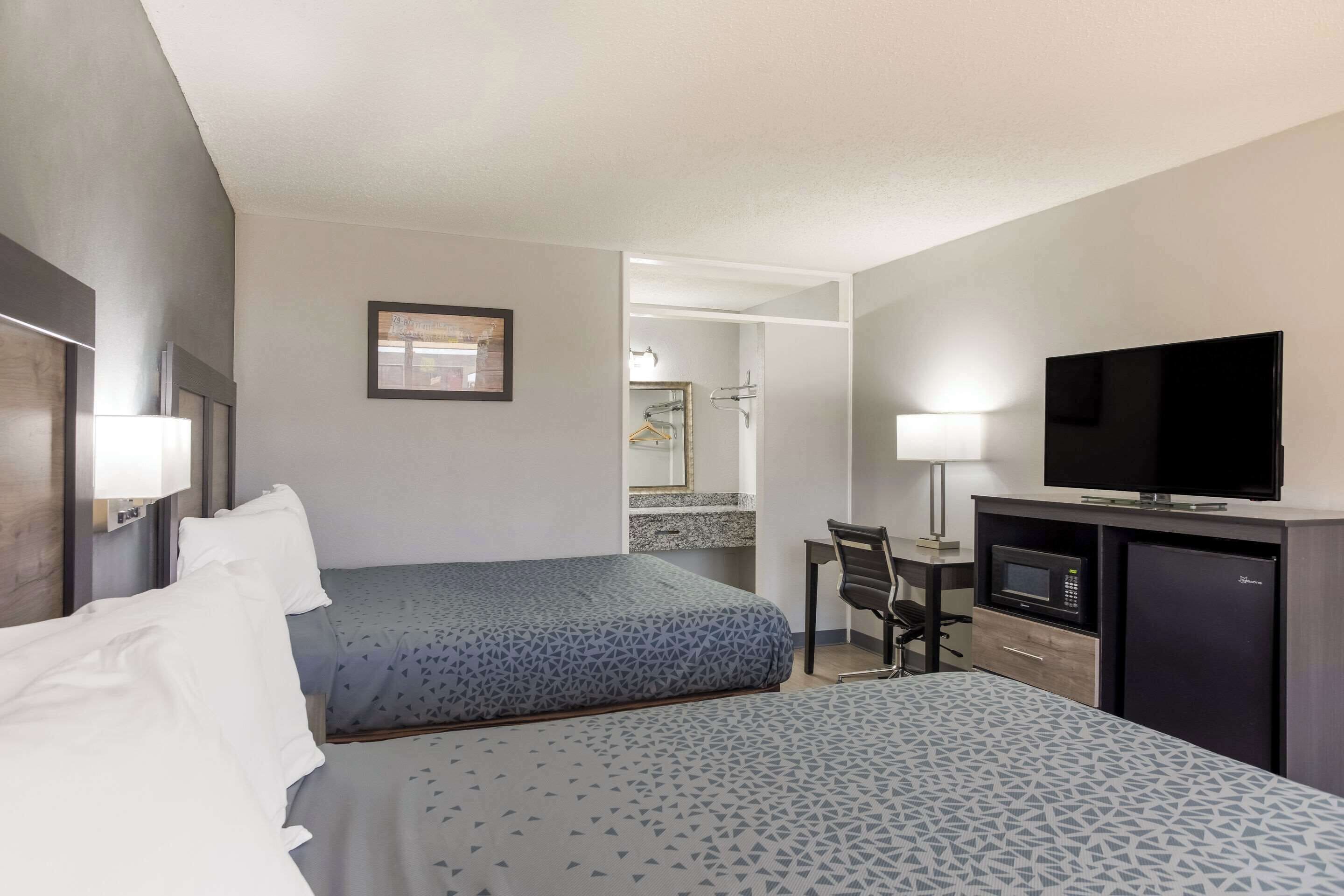 Une chambre d’hôtel avec deux lits, un bureau avec une chaise, une télévision et un four à micro-ondes.