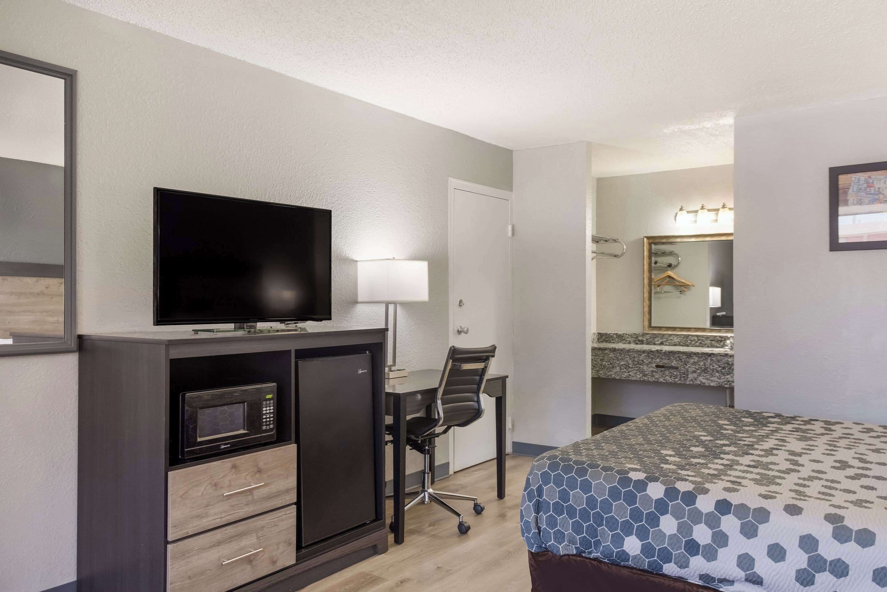 A hotel room with a bed, a desk with a chair, a television, a microwave, and a mirror.