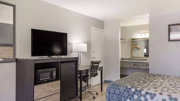 Habitación de hotel con cama, escritorio con silla, televisor, microondas y espejo.