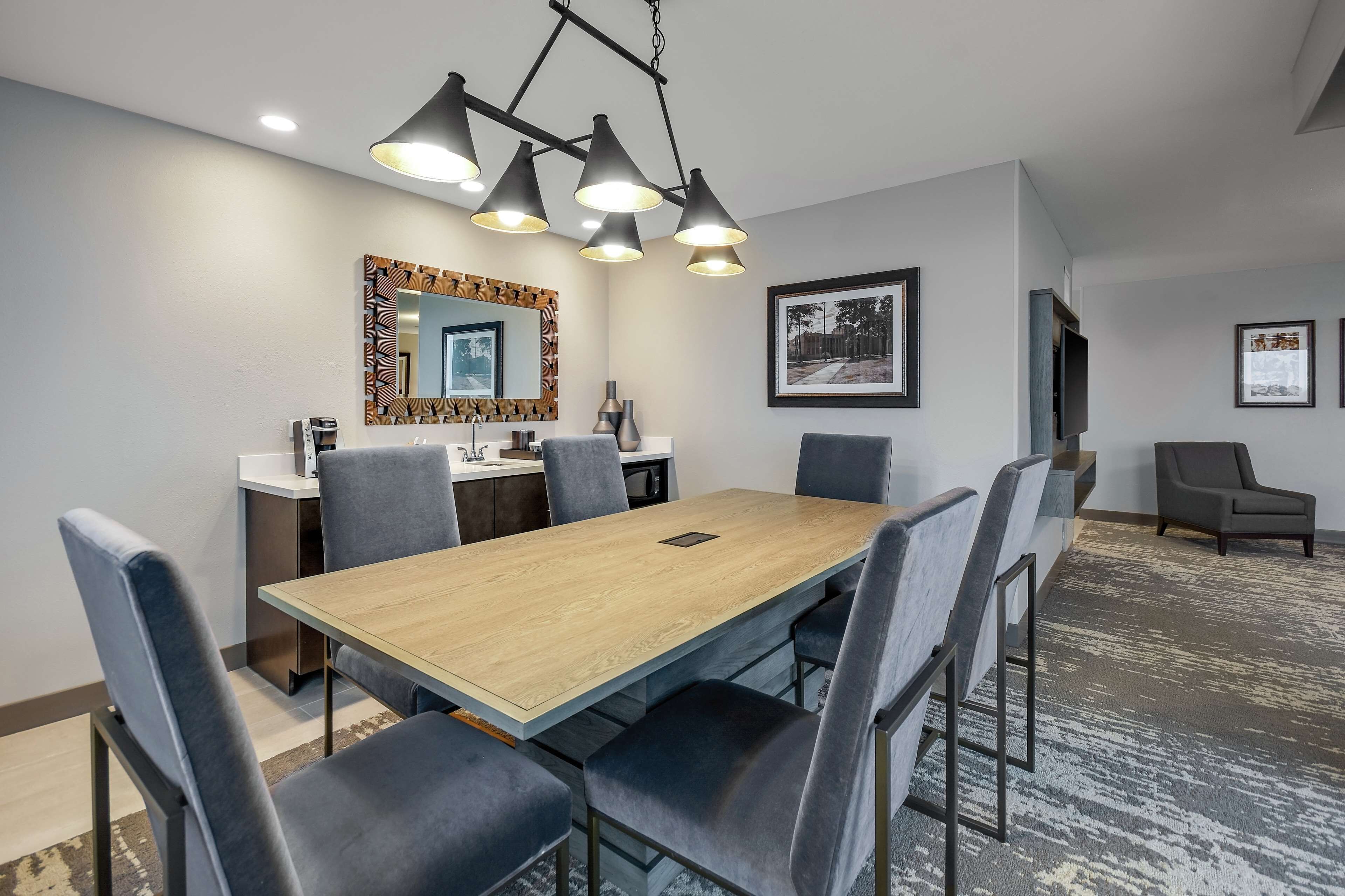 A modern dining area with a wooden table and grey upholstered chairs, a large mirror, and a ceiling light fixture.