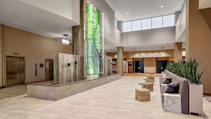 A spacious lobby with a modern design, featuring a central vertical garden, multiple elevators, and a seating area with a plant.