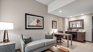 A modern living room with a grey sofa, a small table, and a coffee table. There is a kitchen area with a counter and a sink.