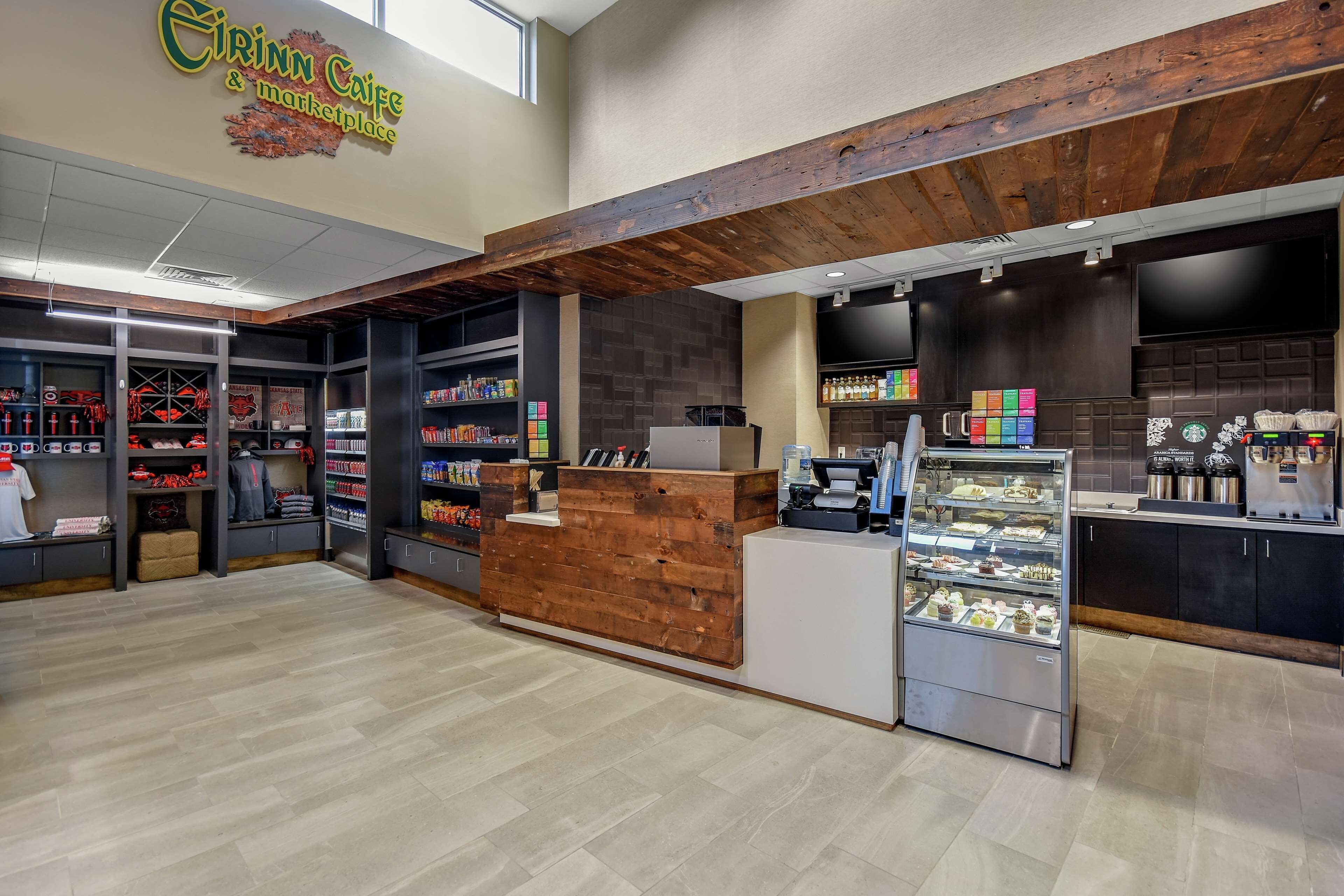 A store interior with a wooden reception desk, shelves stocked with various products, and a display case with pastries.