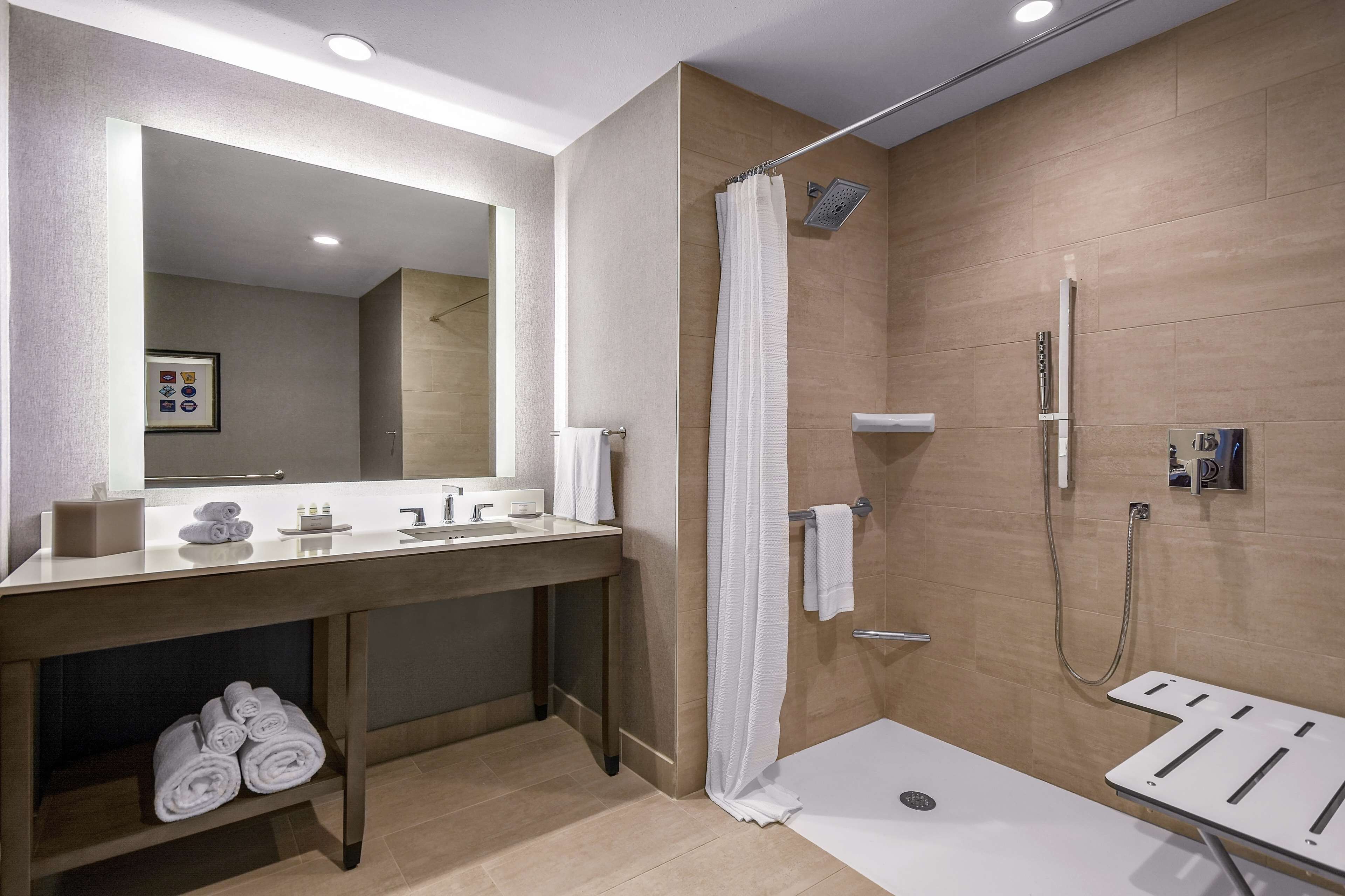 A modern bathroom with a large mirror, a wooden vanity, a shower with a glass door, and a white towel rack.