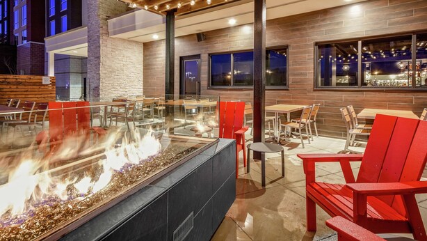 An outdoor seating area with a fire feature, red chairs, and a modern building facade with large windows.