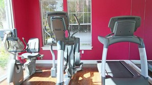 A gym with cardio machines, including an elliptical, a stationary bike, and a treadmill, against a red wall with a window. - Mickey an Minnie House (Kissimmee)