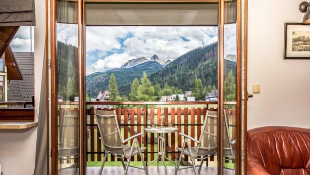 A balcony with a table and chairs, a red leather chair, and a mountain view. - Giewont View by Interhome (Zakopane)