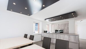 Una cocina moderna con una isla central, una zona de comedor con una mesa larga y sillas, e iluminación empotrada en el techo.