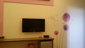 A room with a flat-screen TV mounted on the wall, a small desk with a computer and a cup, and a decorative wall with floral patterns and text. - Stone Home Bed and Breakfast (Taitung)
