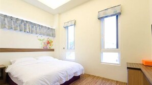A bedroom with a bed, two windows, a nightstand, and a wooden headboard. - Stone Home Bed and Breakfast (Taitung)