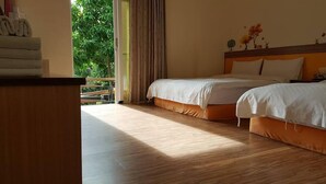 A hotel room with two beds, a wooden floor, a balcony with curtains, and a view of greenery outside. - Stone Home Bed and Breakfast (Taitung)