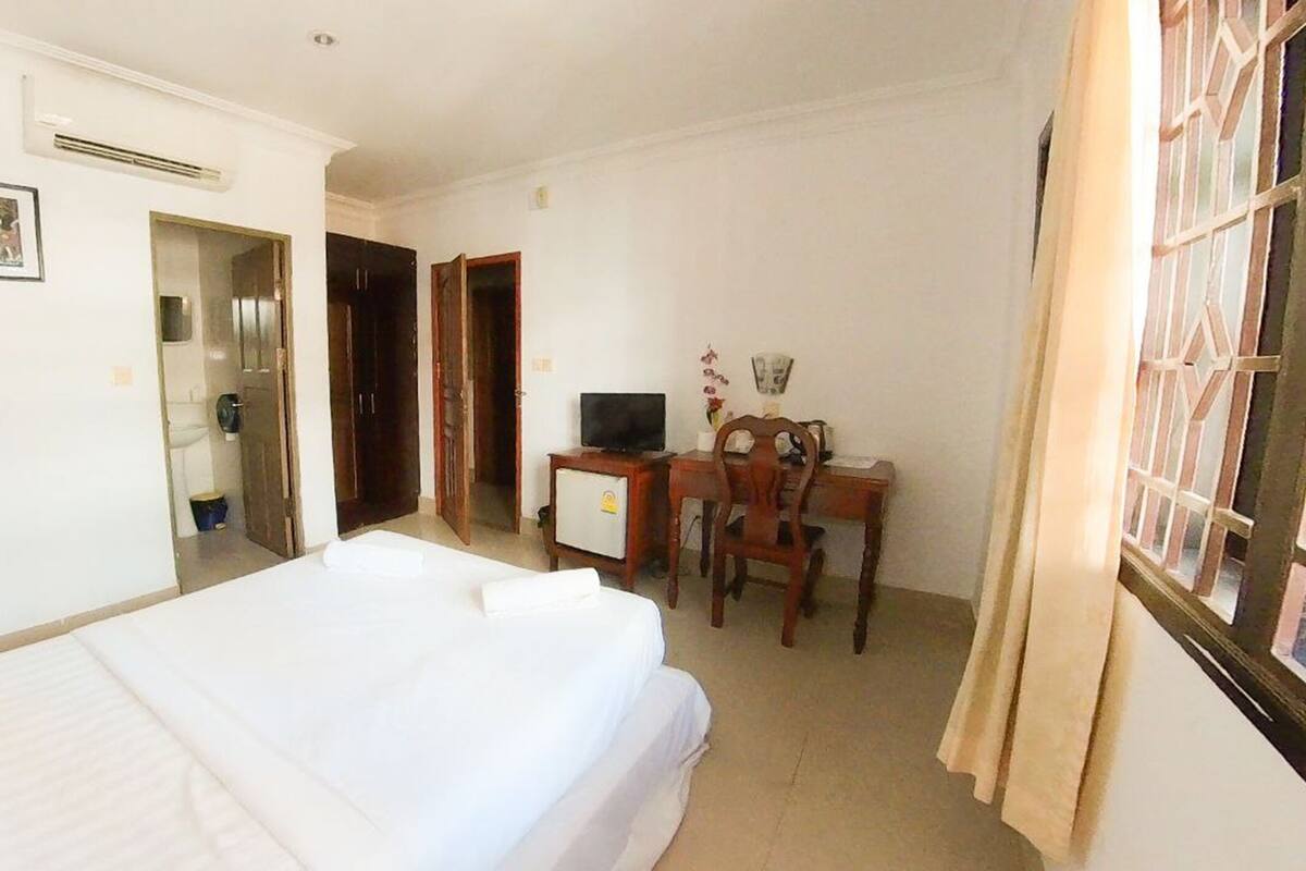 Une chambre d’hôtel comprenant un lit, un bureau avec une chaise, une télévision et une fenêtre avec des rideaux.