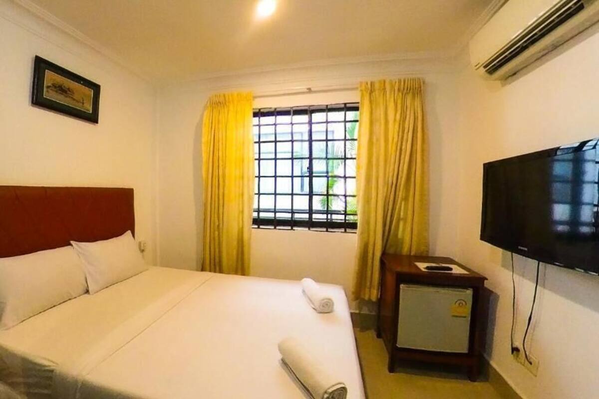 Une chambre d’hôtel avec un lit, une télévision, une petite table et une fenêtre avec des rideaux.
