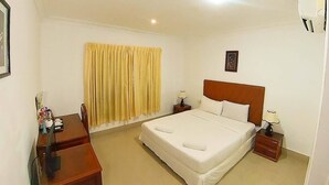 Ein Hotelzimmer mit einem großen Bett, zwei Nachttischen, einem Schreibtisch und einem Fenster mit Vorhängen.