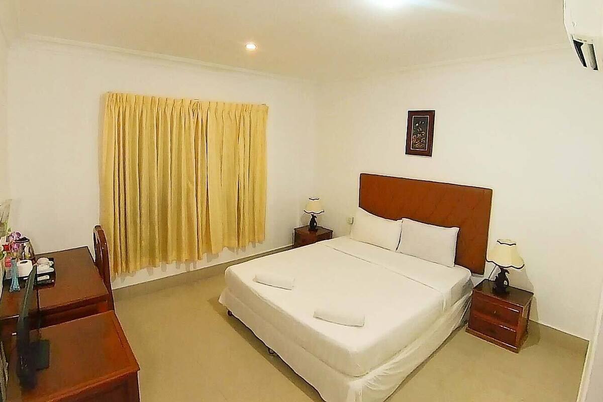 Une chambre d’hôtel avec un grand lit, deux tables de chevet, un bureau et une fenêtre avec des rideaux.