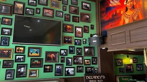 Ein Restaurant mit grüner Wand, verziert mit gerahmten Fotos, einem Flachbildfernseher und einem Deckenventilator.
