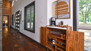 A hallway with wooden flooring, a coffee station with a coffee maker and cups, and a wall-mounted artwork.