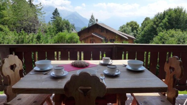 A wooden table with four white cups and saucers, a spoon, and a rock centerpiece on a balcony with a wooden railing. - Le Mont Blanc 8 by Interhome (Villars)