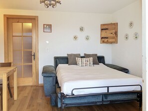 A bedroom with a bed, a wooden door, a small table, and decorative wall plates. - Le Mont Blanc 8 by Interhome (Villars)